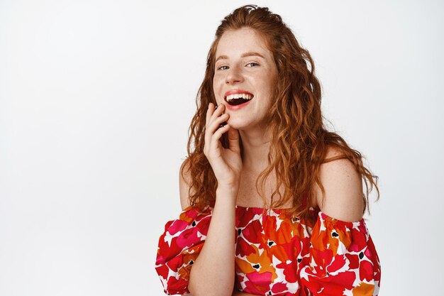 Portrait d'une belle femme rousse riant et souriant montrant des émotions franches posant en robe sur fond blanc