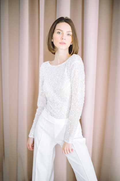 Portrait de la belle femme à la salle avec perle debout et à la recherche en chemise blanche et pantalon