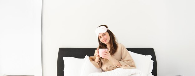 Portrait d'une belle femme se relaxant au lit, se réveillant et prenant sa tasse de café du matin
