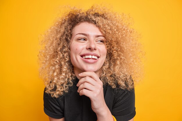 Portrait d'une belle femme sincère garde la main sur le menton sourit largement détourne le regard exprime des émotions authentiques