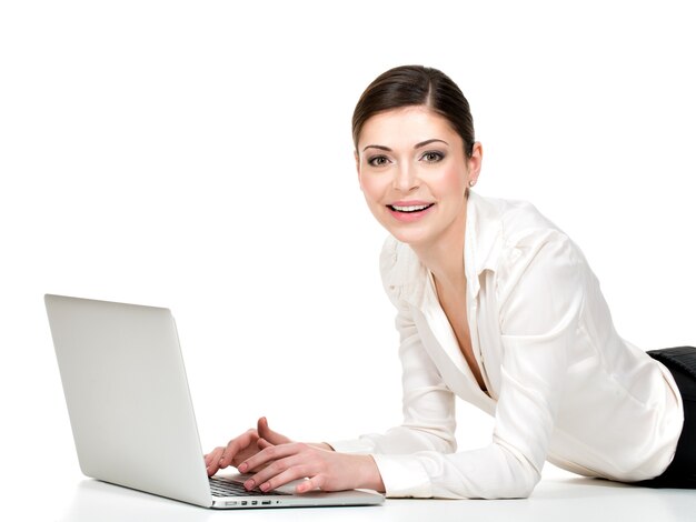 Portrait d'une belle femme souriante avec ordinateur portable en chemise blanche allongée sur le sol - isolé sur blanc.