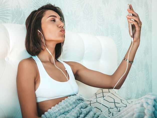 Portrait d'une belle femme souriante vêtue d'un pyjama blanc et écoutant de la musique avec des écouteurs