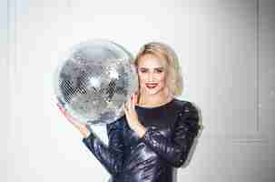 Photo gratuite portrait de la belle femme tenant une boule disco sur un mur blanc