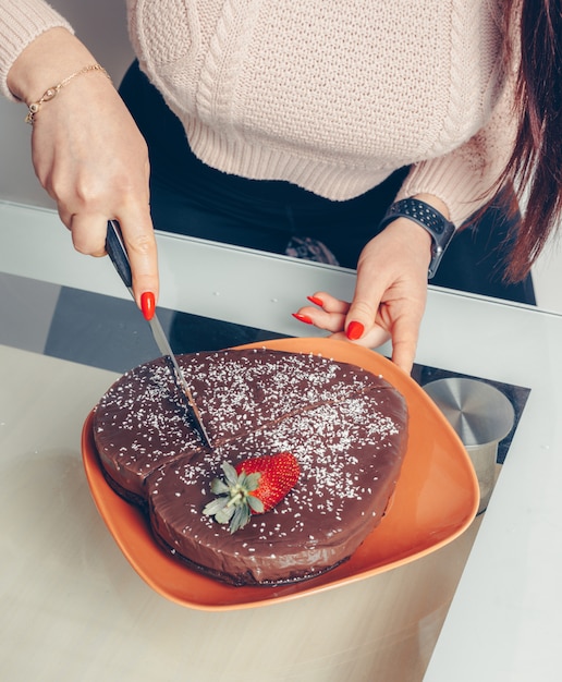 Photo gratuite portrait de belle femme trancher le gâteau en forme de coeur et en rose saumon crop top à la chambre.