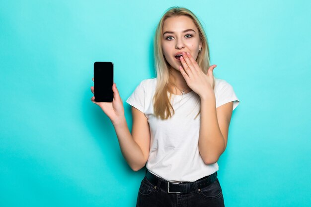 Portrait d'une belle fille excitée = doigt pointé sur un téléphone mobile à écran blanc isolé sur mur bleu