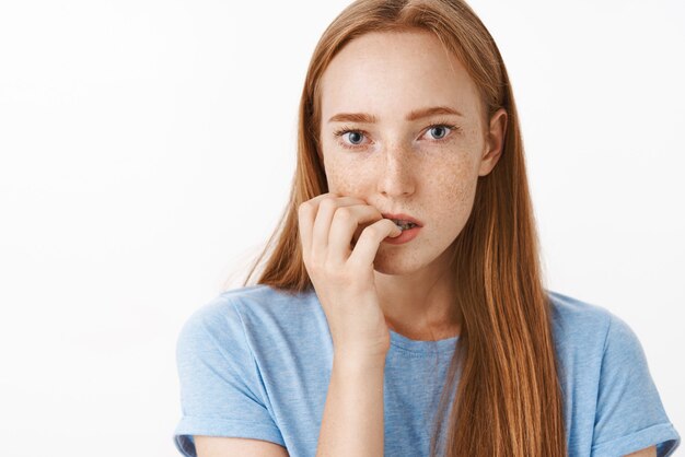 Portrait de belle fille gingembre focalisée concernée avec des taches de rousseur se mordant les ongles de sentiment nerveux et de panique en attente de punition pour fumer