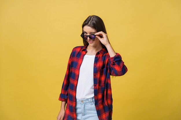 Portrait d'une belle fille à lunettes rondes sur fond jaune en studio.