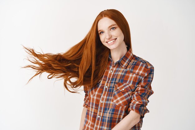 Portrait de belle fille rousse gaie avec des cheveux bouclés volants souriant en riant regardant de côté sur fond blanc