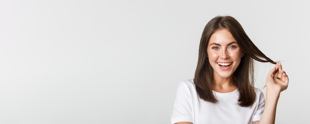 Portrait d'une belle fille séduisante jouant avec les cheveux et souriant à la caméra intriguée