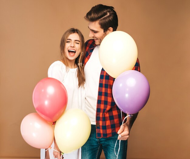 Portrait de belle fille souriante et son beau petit ami tenant des tas de ballons colorés et riant. Couple heureux en amour. Bon anniversaire