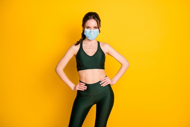 Portrait d'une belle fille sportive mince et gaie instructeur de pilates mains sur les hanches porter un masque isolé sur fond de couleur jaune vif