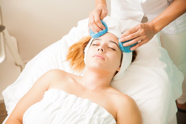 Portrait d'une belle jeune brune se relaxant lors d'un soin du visage hydratant dans un spa