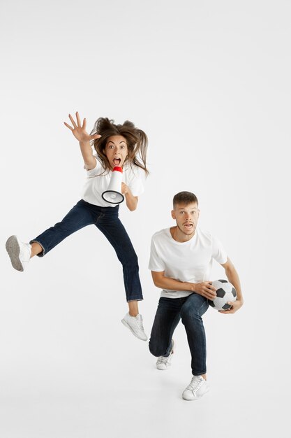 Portrait de la belle jeune couple de fans de football ou de football sur un mur blanc. Expression faciale, émotions humaines, publicité, concept sportif. Femme et homme sautant, criant, s'amusant.