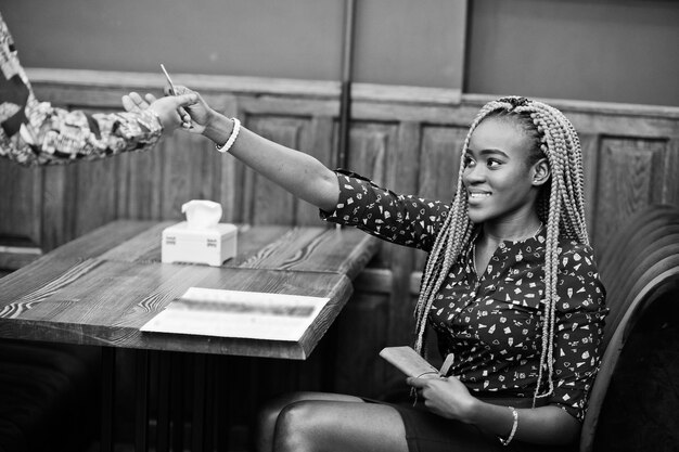 Portrait d'une belle jeune femme d'affaires africaine portant un chemisier bleu et une jupe assis au restaurant et donne une carte de crédit au serveur afro girl