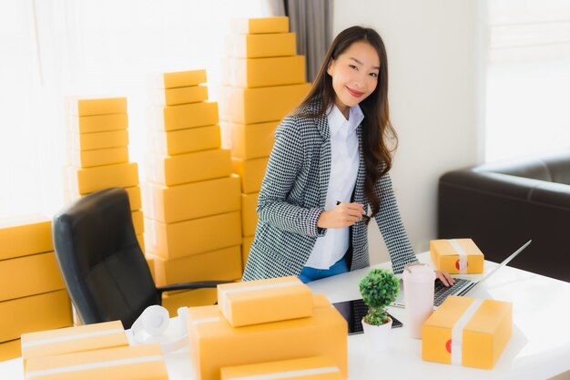 Portrait belle jeune femme d'affaires asiatique travail à domicile avec ordinateur portable téléphone portable avec boîte en carton prêt pour l'expédition