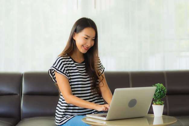 Portrait de la belle jeune femme asiatique à l'aide d'un ordinateur portable sur le canapé