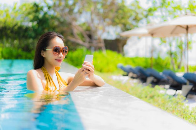 Portrait belle jeune femme asiatique à l&#39;aide de téléphone portable ou téléphone portable dans la piscine