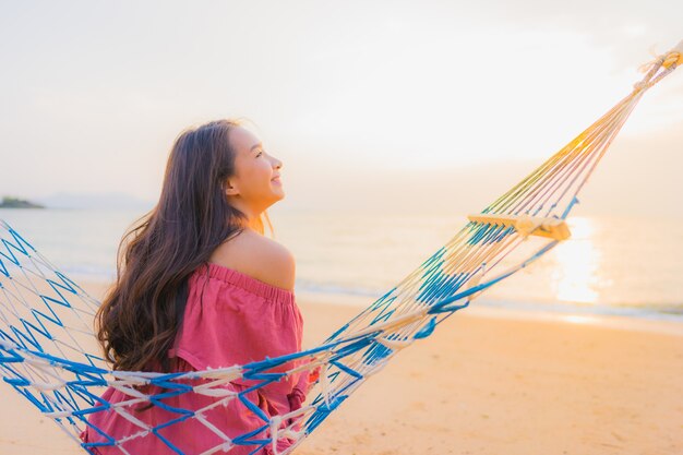 Portrait belle jeune femme asiatique assise sur le hamac avec sourire heureux neary plage mer et oce