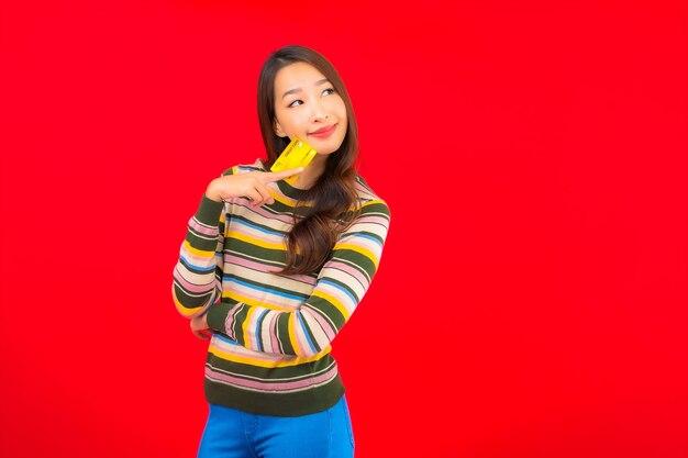 Portrait belle jeune femme asiatique avec carte de crédit sur mur isolé rouge