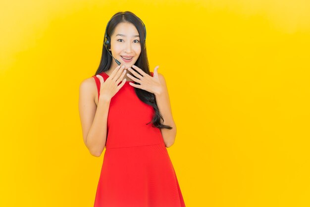 Portrait belle jeune femme asiatique avec casque pour la communication et le service de centre d'appels de soutien sur le mur jaune