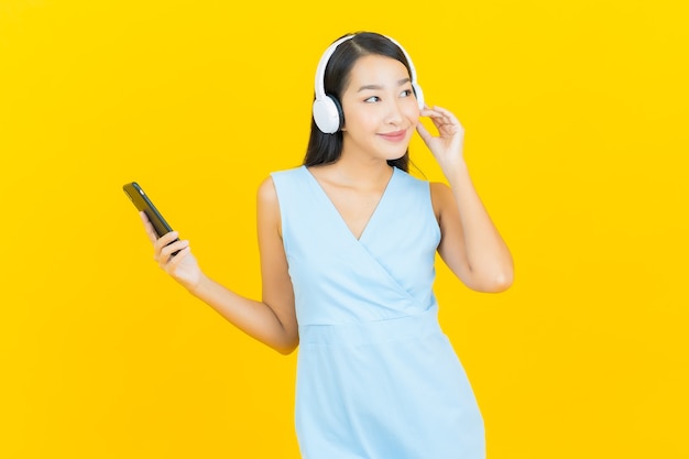 Portrait belle jeune femme asiatique avec casque et téléphone intelligent pour écouter de la musique sur le mur jaune