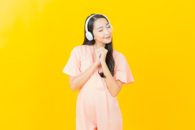 Portrait belle jeune femme asiatique avec casque et téléphone intelligent pour écouter de la musique sur le mur jaune