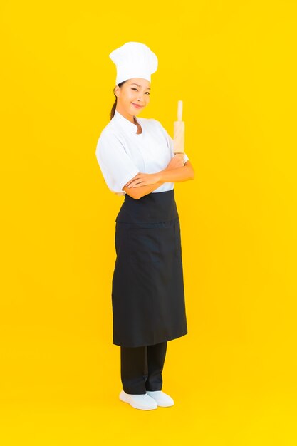 Portrait belle jeune femme asiatique chef avec rouleau à pâtisserie sur fond isolé jaune