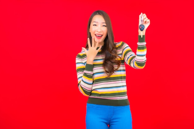 Portrait belle jeune femme asiatique avec clé de voiture sur mur isolé rouge