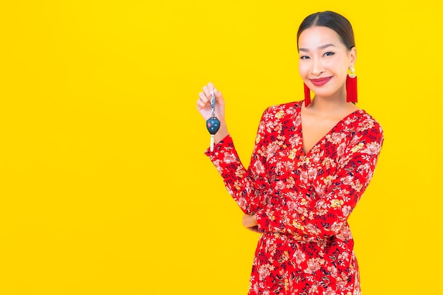 Photo gratuite portrait belle jeune femme asiatique avec clé de voiture sur mur jaune