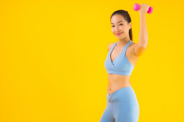 Portrait belle jeune femme asiatique avec haltère et vêtements de sport sur jaune