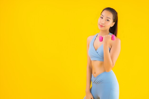 Portrait belle jeune femme asiatique avec haltère et vêtements de sport sur jaune