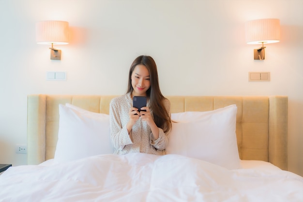 Portrait belle jeune femme asiatique sur le lit avec téléphone mobile intelligent