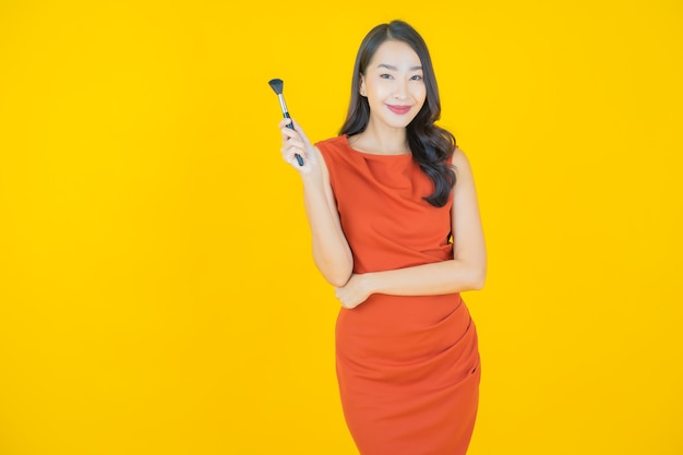 Portrait belle jeune femme asiatique avec maquillage pinceau cosmétique sur jaune