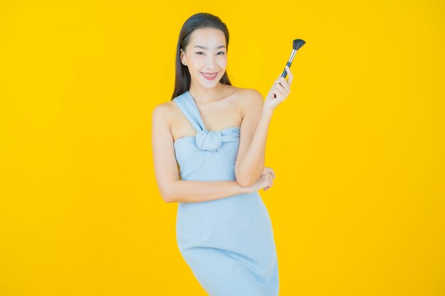 Portrait belle jeune femme asiatique avec maquillage pinceau cosmétique sur jaune