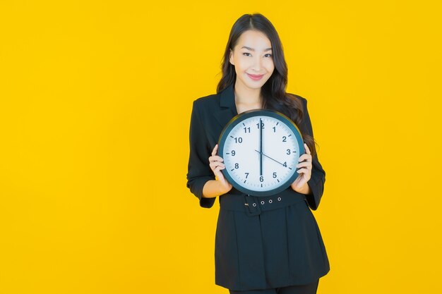 Portrait belle jeune femme asiatique montre une alarme ou une horloge sur jaune jaune