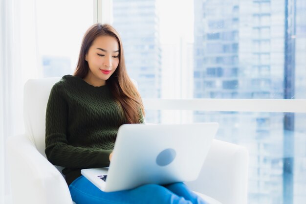 Portrait belle jeune femme asiatique avec ordinateur portable et tasse de café sur le canapé