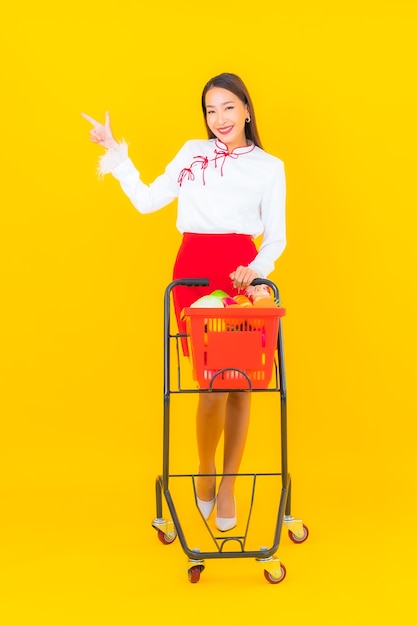 Portrait belle jeune femme asiatique avec panier d'épicerie de supermarché sur jaune