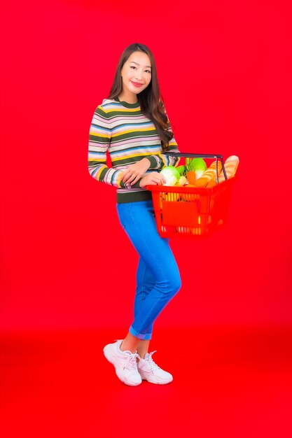 Portrait belle jeune femme asiatique avec panier d'épicerie de supermarché sur mur isolé rouge