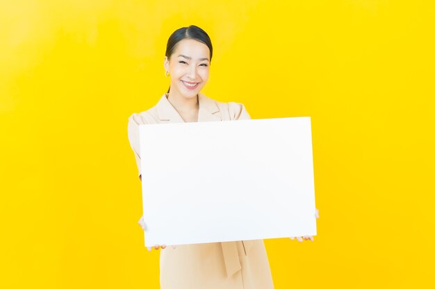 Portrait belle jeune femme asiatique avec panneau d'affichage blanc vide sur mur de couleur