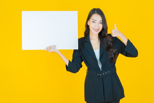 Portrait belle jeune femme asiatique avec panneau blanc vide sur jaune