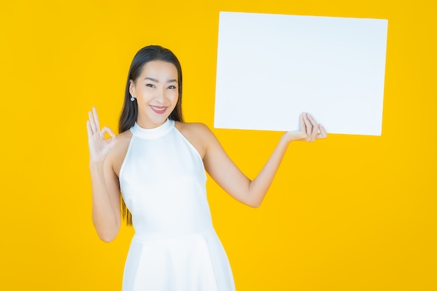 Portrait belle jeune femme asiatique avec panneau blanc vide sur jaune