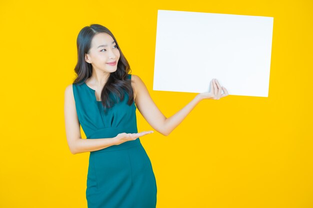 Portrait belle jeune femme asiatique avec panneau blanc vide sur jaune