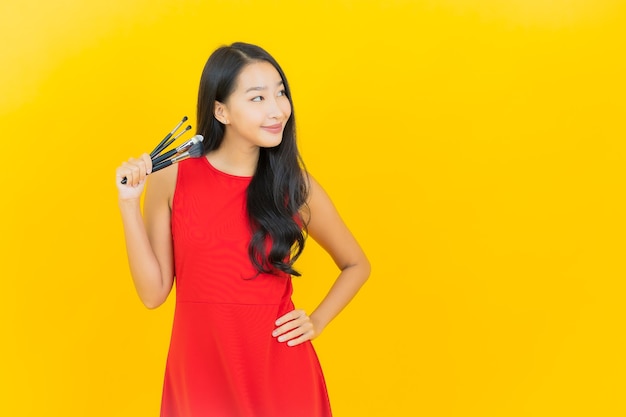 Portrait belle jeune femme asiatique avec pinceau cosmétique sur mur jaune