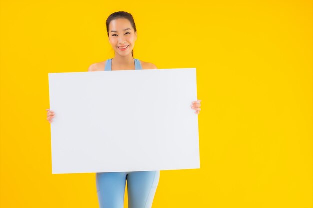 Portrait belle jeune femme asiatique porter des vêtements de sport afficher un panneau d'affichage blanc vide sur jaune