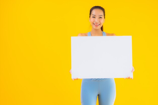 Portrait belle jeune femme asiatique porter des vêtements de sport afficher un panneau d'affichage blanc vide sur jaune