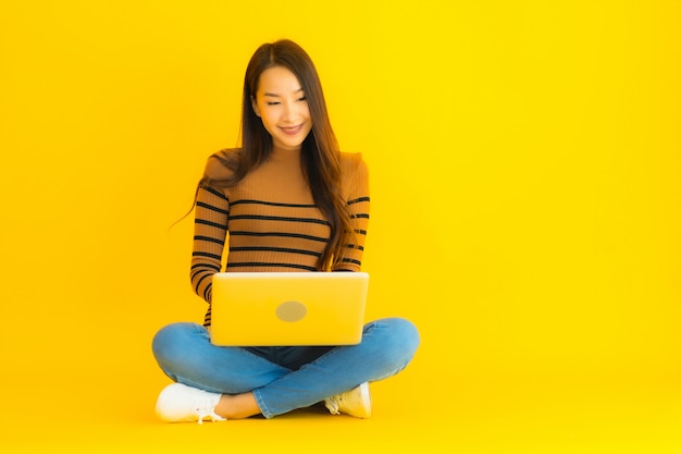 Portrait belle jeune femme asiatique s'asseoir sur le sol pour utiliser un ordinateur portable ou un ordinateur sur le mur jaune