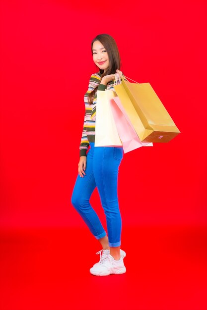 Portrait belle jeune femme asiatique avec sac à provisions coloré sur mur rouge