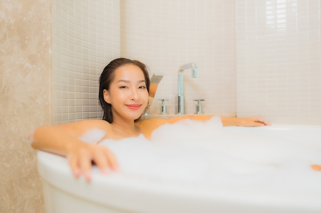 Portrait belle jeune femme asiatique se détendre sourire dans la baignoire à l'intérieur de la salle de bain