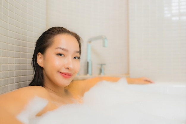 Portrait belle jeune femme asiatique se détendre sourire dans la baignoire à l'intérieur de la salle de bain
