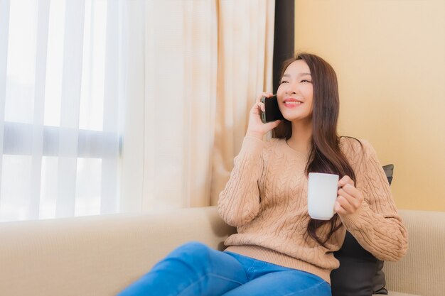 Portrait belle jeune femme asiatique se détendre sourire heureux avec un téléphone intelligent avec du café sur le canapé